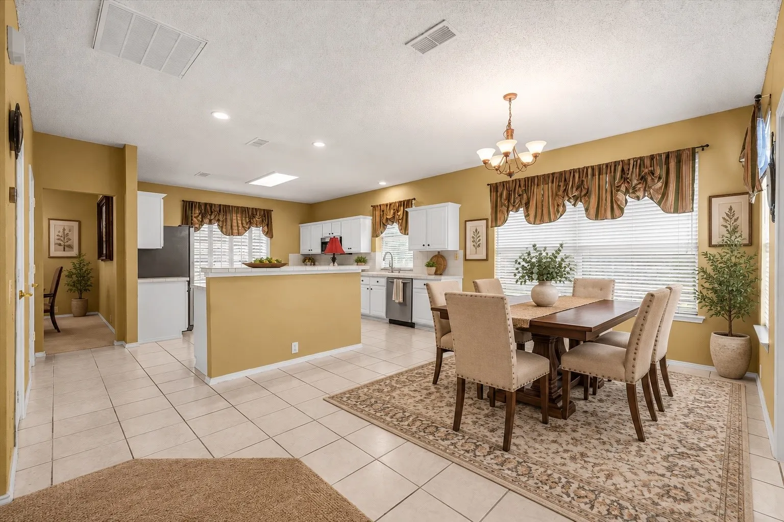 Recessed lighting, tile flooring, white cabinetry, integrated kitchen island, and a dining area with a chandelier