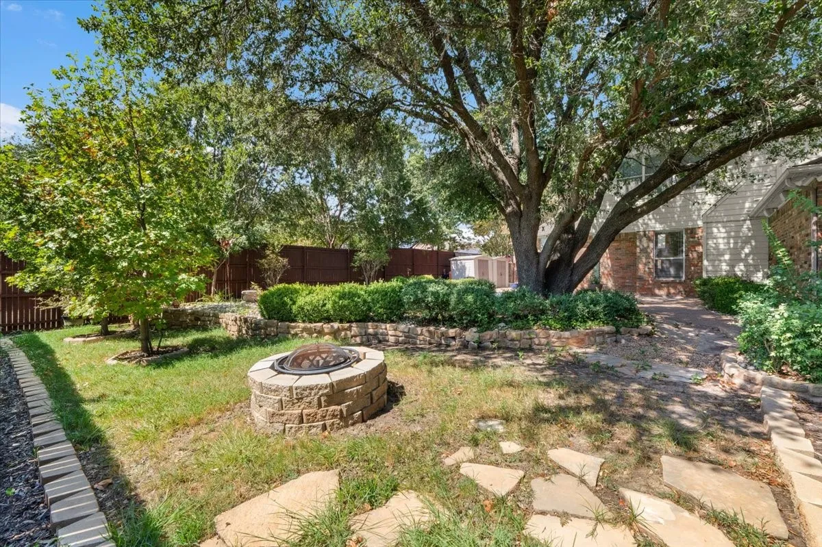 Terraced landscaping with a stone fire pit, mature shade trees, and a privacy fence