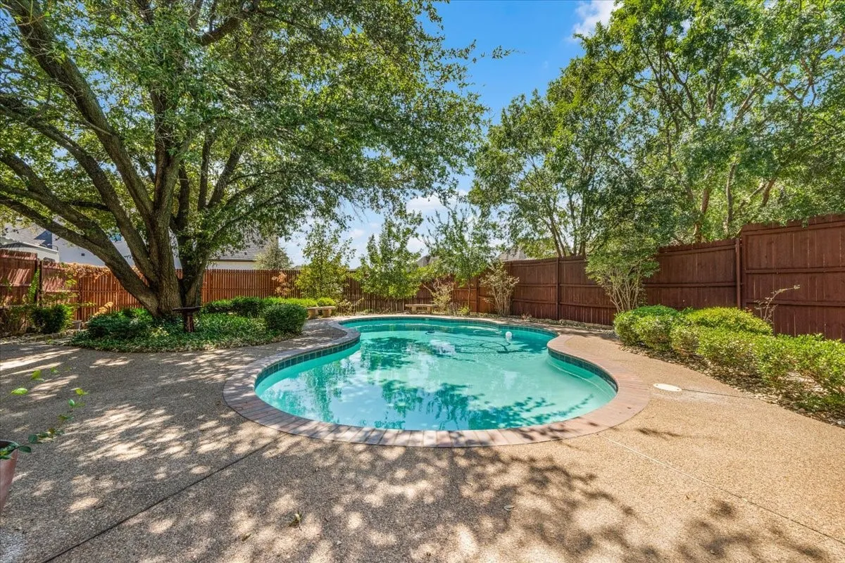 Curved swimming pool with a brick coping, surrounded by an exposed aggregate patio