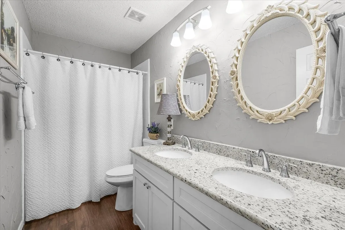 Dual vanity with white cabinetry, light-toned countertop, two oval framed mirrors, and wood-finish flooring