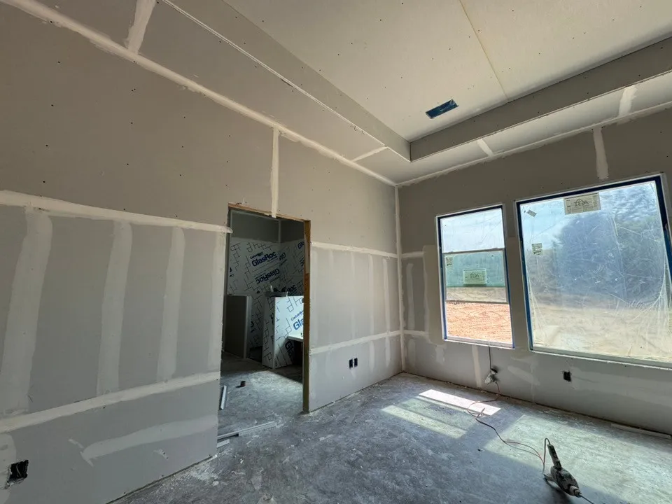 Tray ceiling detail, two large windows, drywall installation, and unfinished flooring