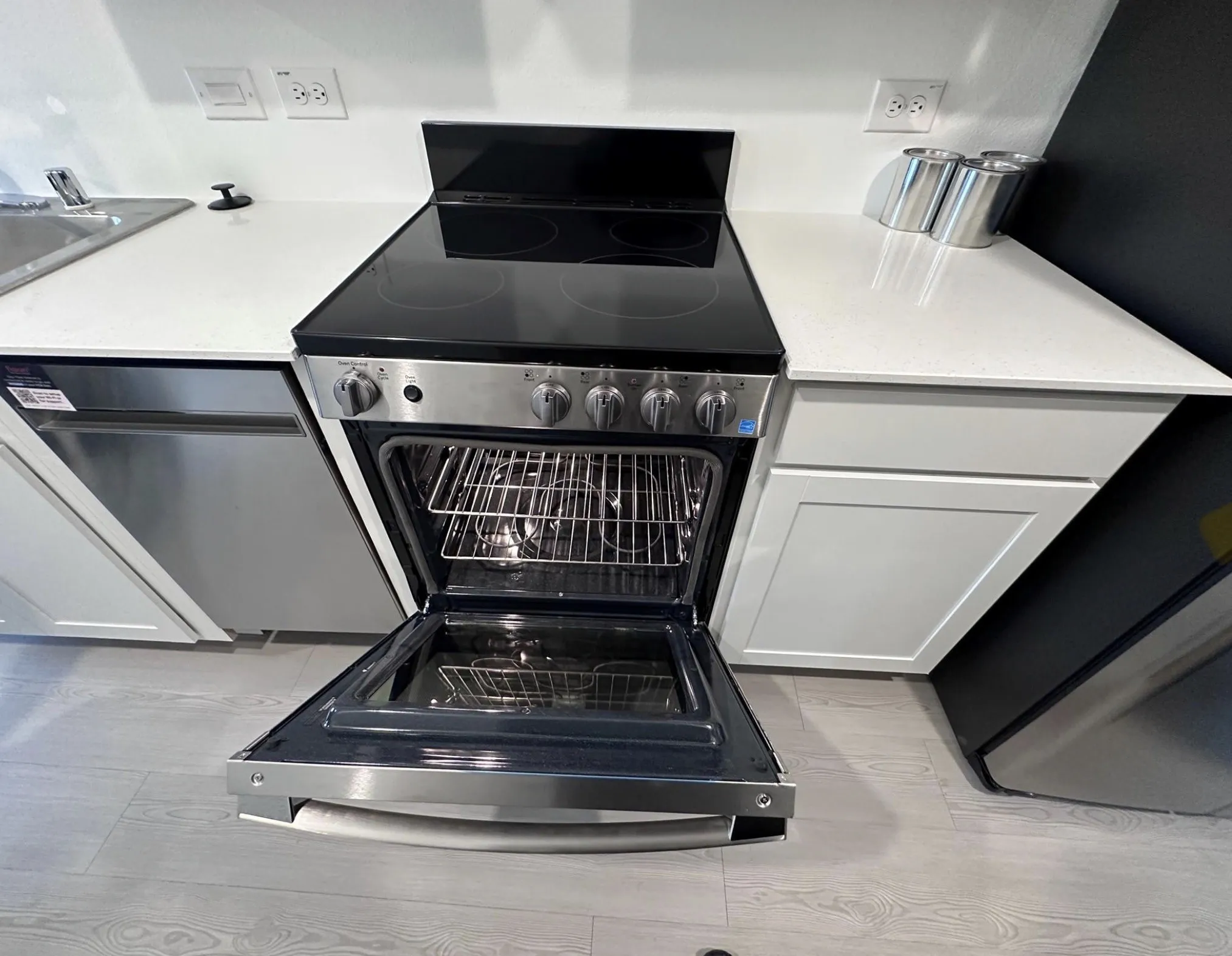 Stainless steel range with an open oven door, integrated into a kitchen featuring white countertops, white shaker-style cabinetry, and wood-finish flooring