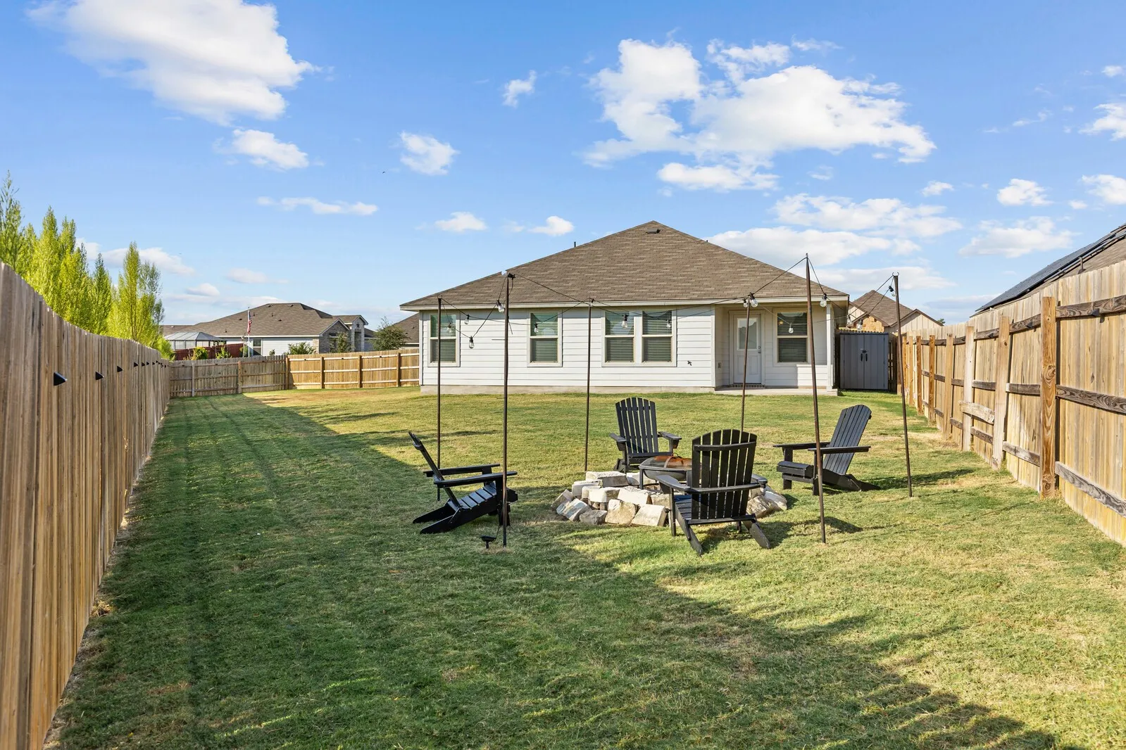 Expansive backyard with a manicured lawn, full wood privacy fencing, and a built-in stone fire pit