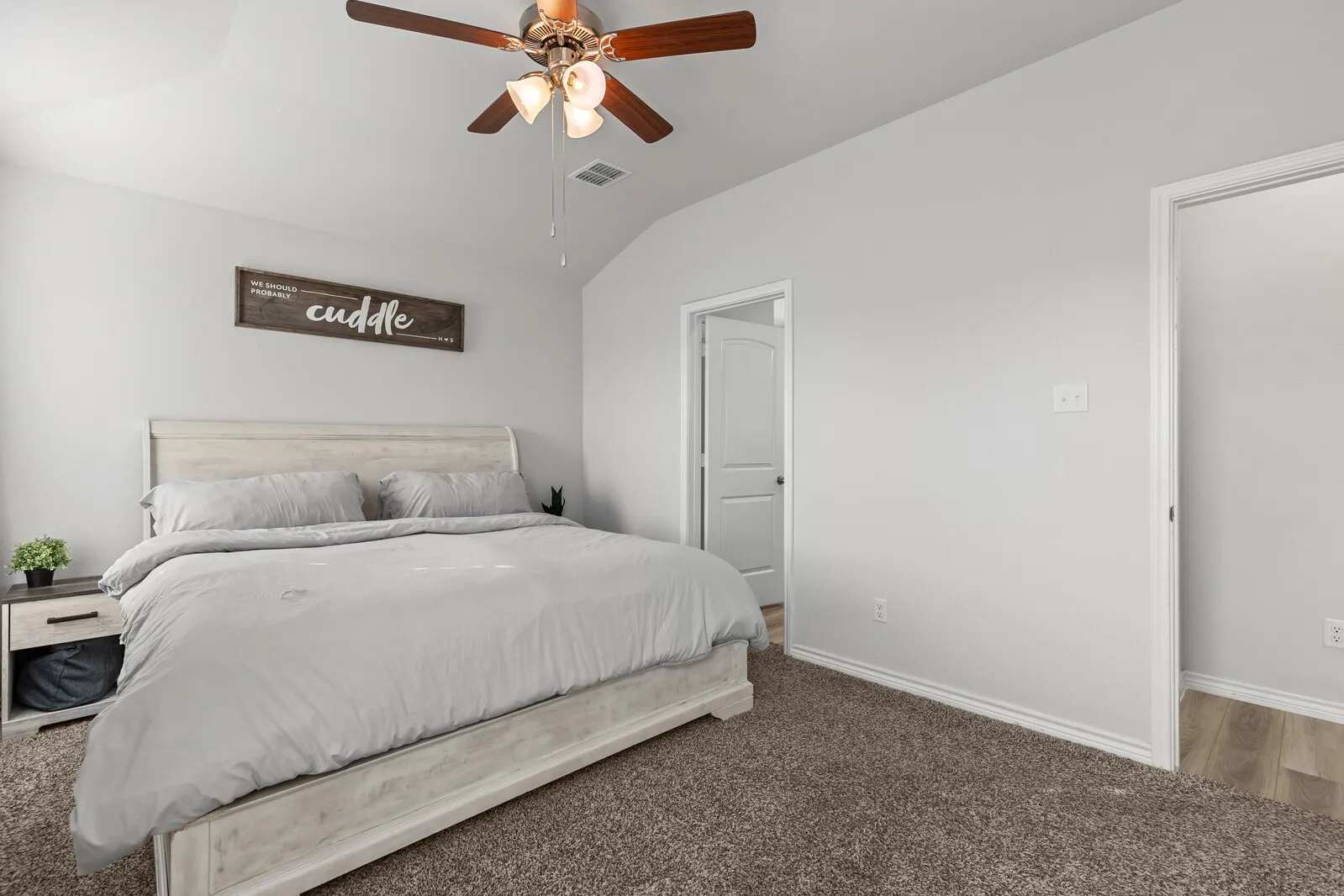Vaulted ceiling with a wood-finish ceiling fan, neutral wall paint, and plush carpeting