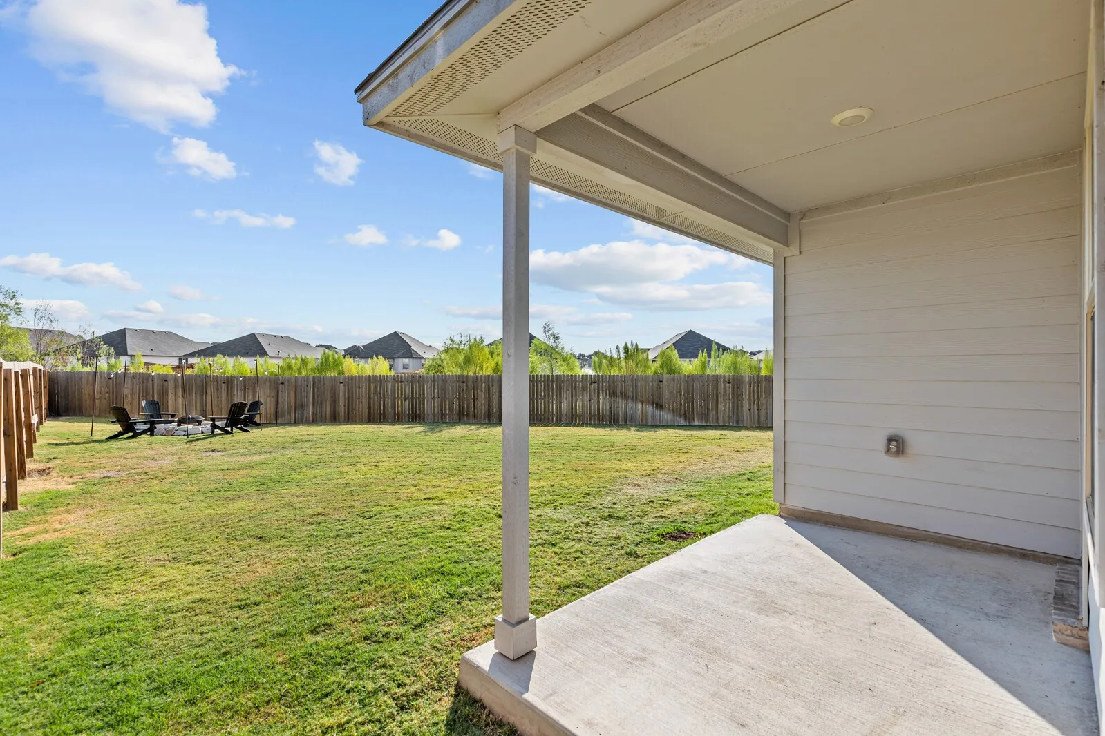 Expansive backyard with a wooden fence, concrete patio, and mature landscaping