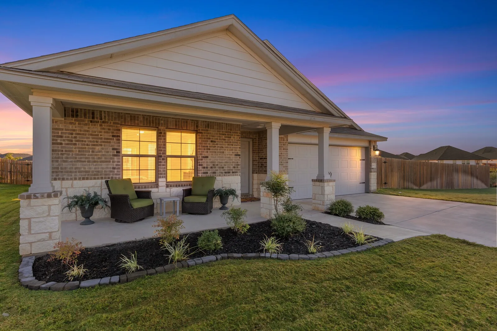 Brick facade with stone accents, covered front porch, attached two-car garage, concrete driveway, and established landscaping