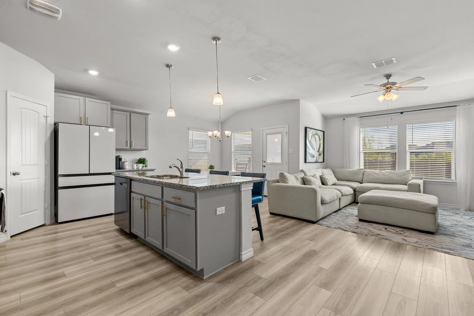 Open-concept layout featuring wood-finish flooring, a kitchen island with granite countertops, light gray cabinetry, and recessed lighting
