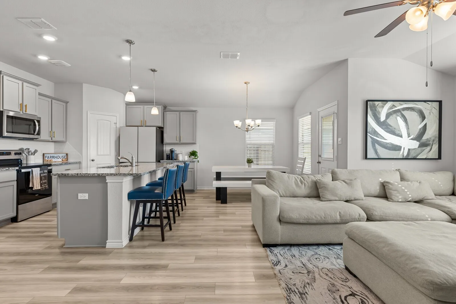 Open-concept living area featuring wood-finish flooring, kitchen island with seating, stainless steel appliances, and vaulted ceilings