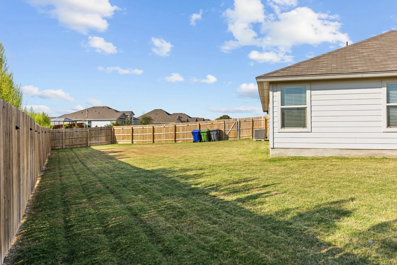 Expansive backyard featuring a wood fence, green lawn, and a siding exterior