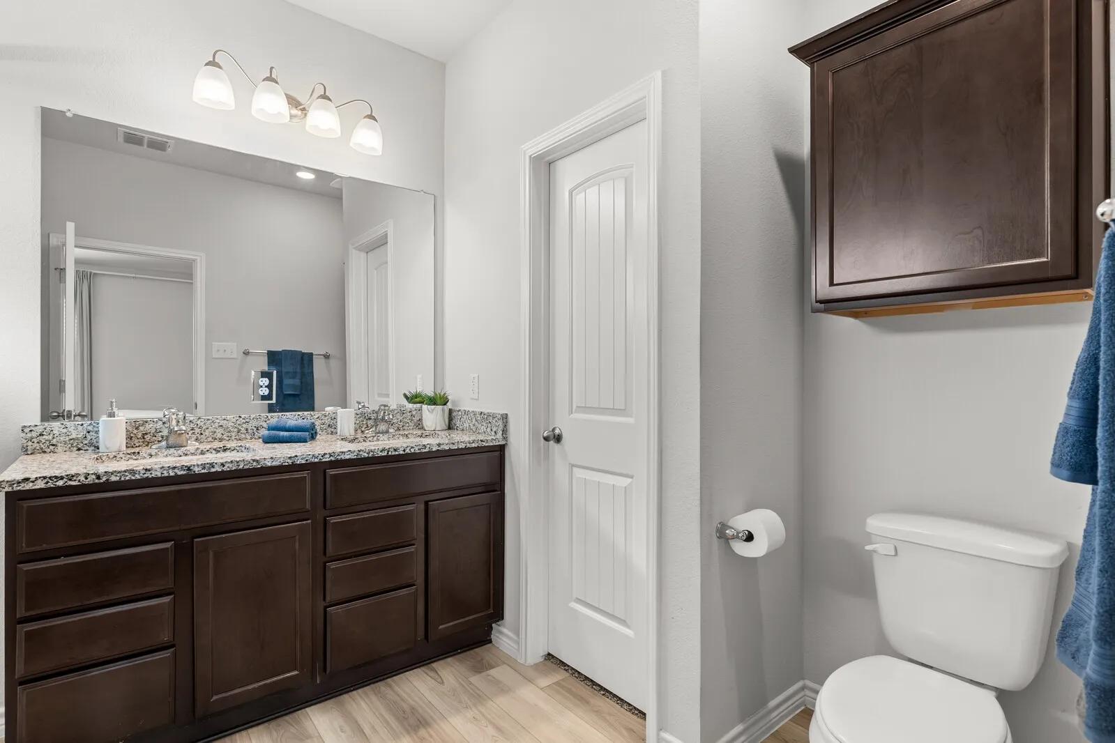 Dual vanity with undermount sinks, granite-patterned countertop, dark wood-finish cabinetry, and wood-finish flooring