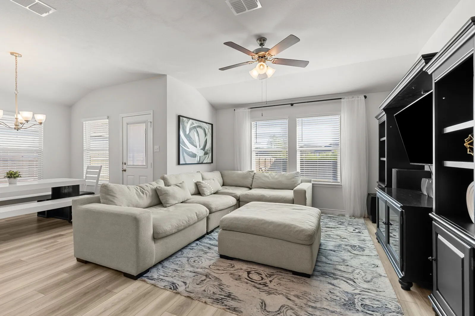 Wood-finish flooring throughout, vaulted ceiling, built-in media console, and a ceiling fan with integrated lighting