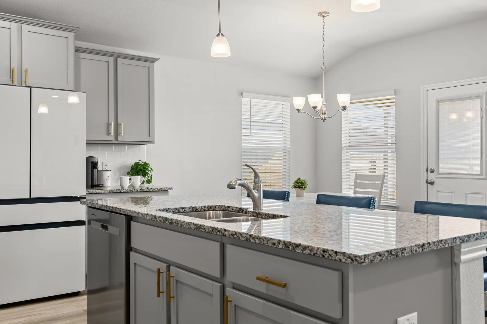 Kitchen featuring light gray cabinetry with gold-tone hardware, granite countertops, a stainless steel sink, and a built-in dishwasher