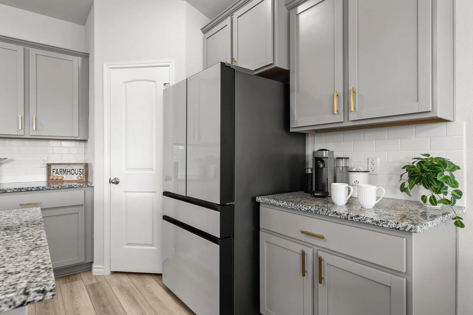Gray cabinetry with gold-tone hardware, granite-style countertops, white subway tile backsplash, and wood-finish flooring