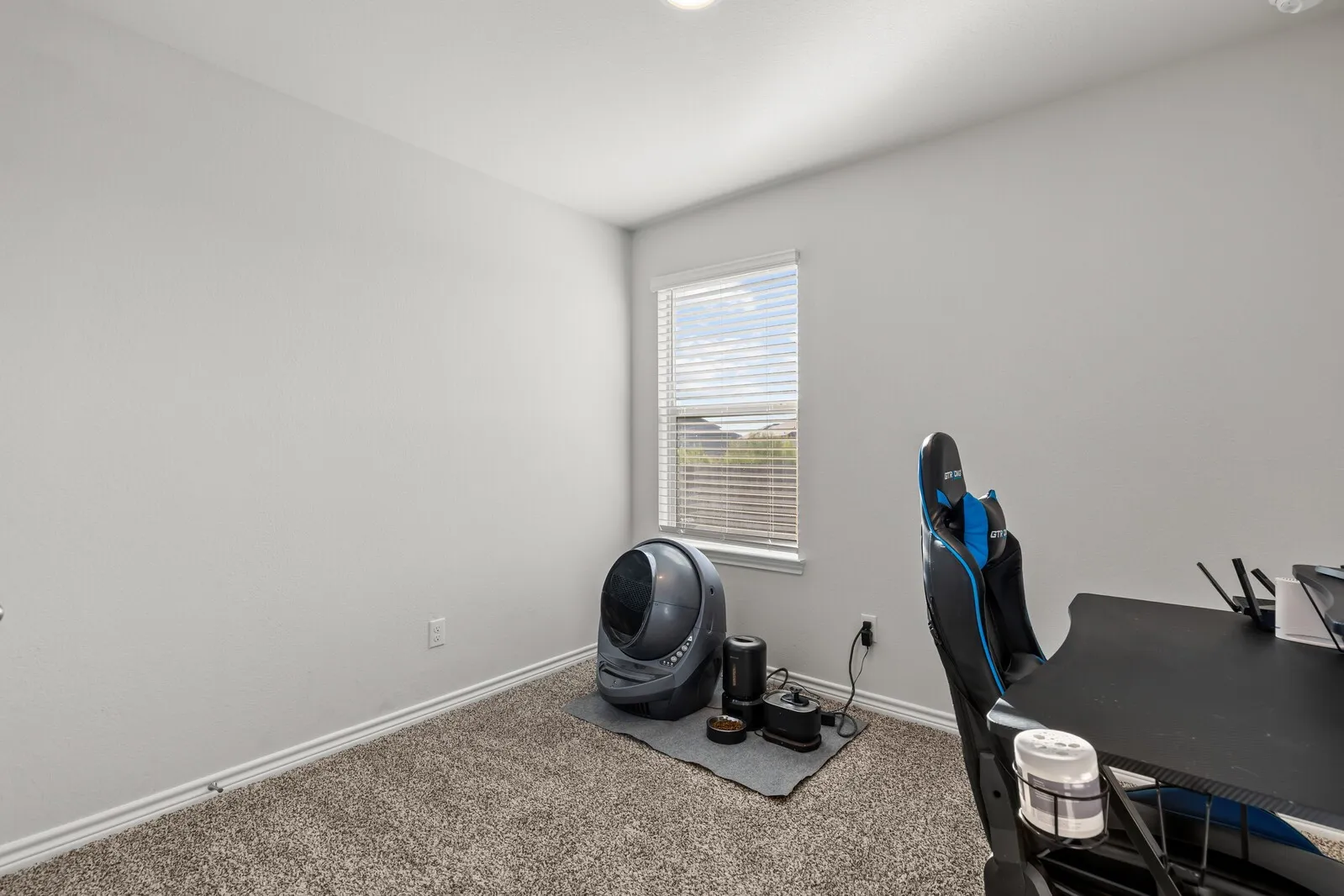 Light gray walls, textured carpeting, and a single window with horizontal blinds (actual room 3)