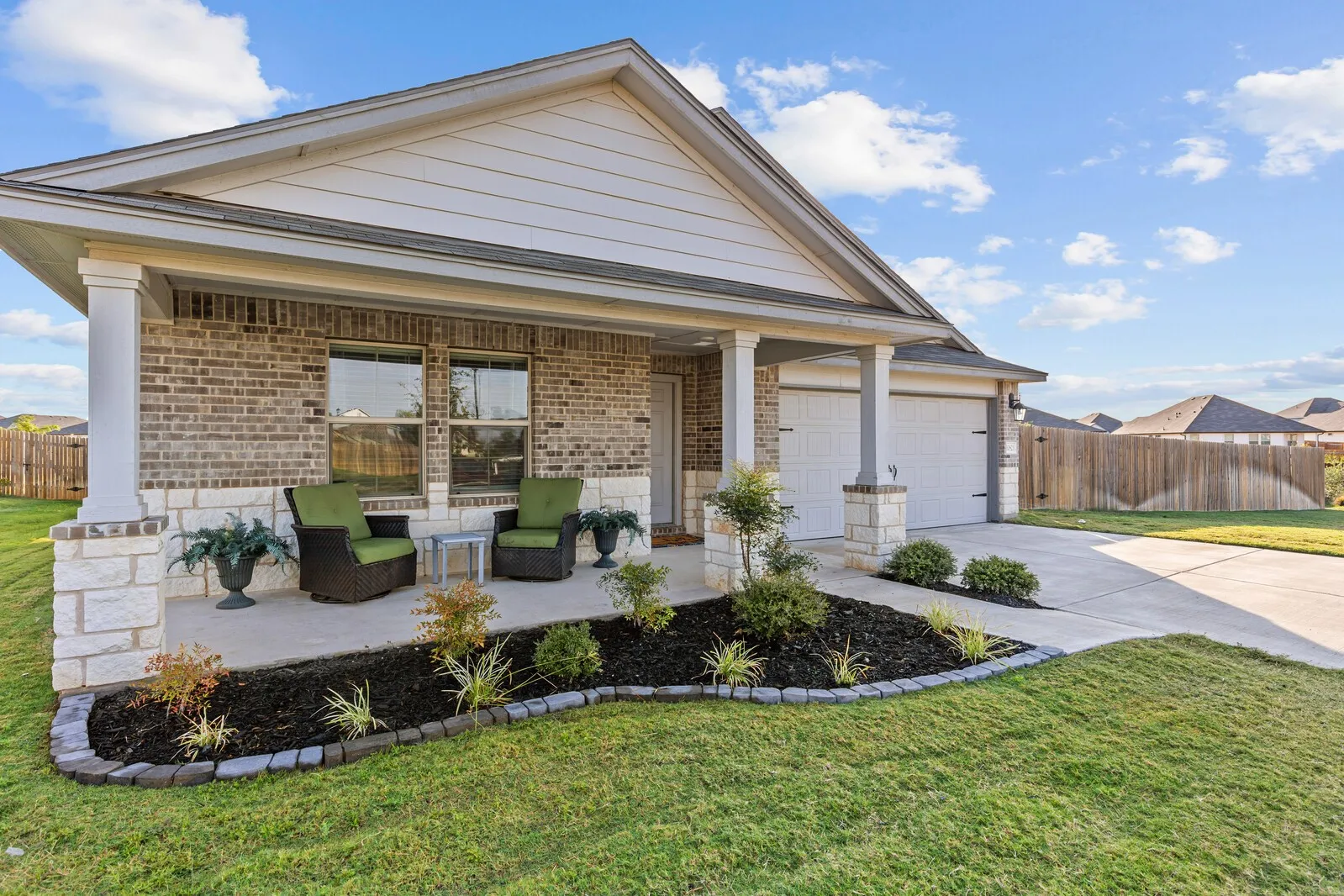 Brick and stone veneer exterior with a covered porch, attached two-car garage, and concrete driveway