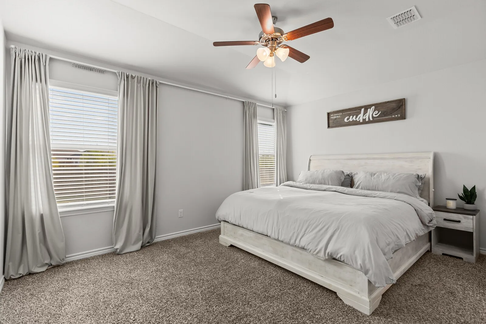 Neutral wall finishes, carpeted flooring, two windows with blinds, and a ceiling fan with integrated lighting (primary bedroom actual)