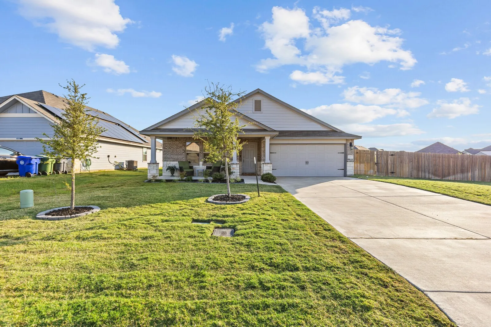 Single-story residence featuring a two-car garage, stone and siding exterior, covered porch, concrete driveway, and a fenced backyard