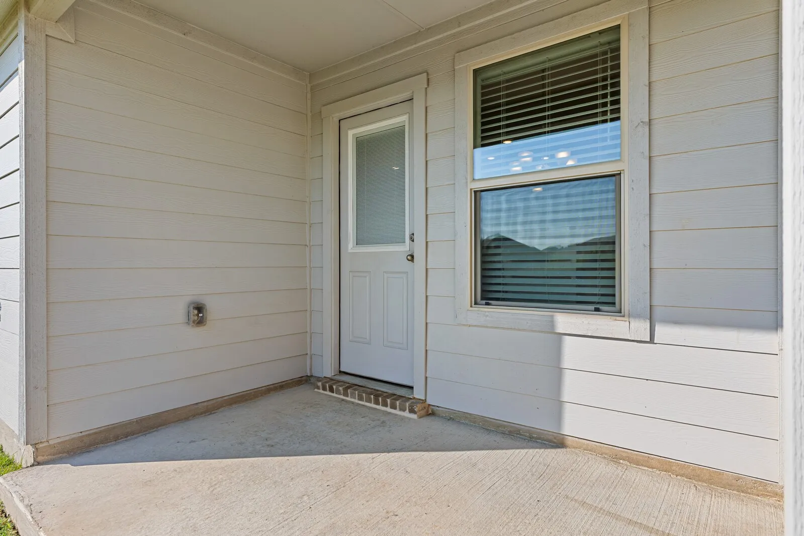 Outdoor concrete patio with a white paneled door and an adjacent window with blinds