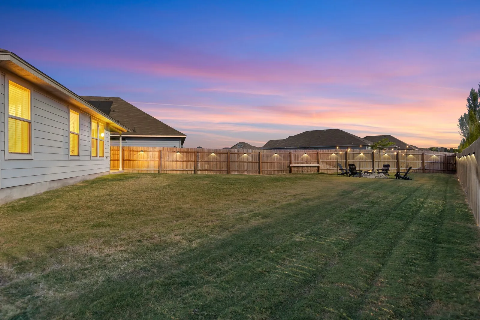 Expansive backyard featuring a wood fence with integrated lighting, a gravel patio area, and a large grass lawn