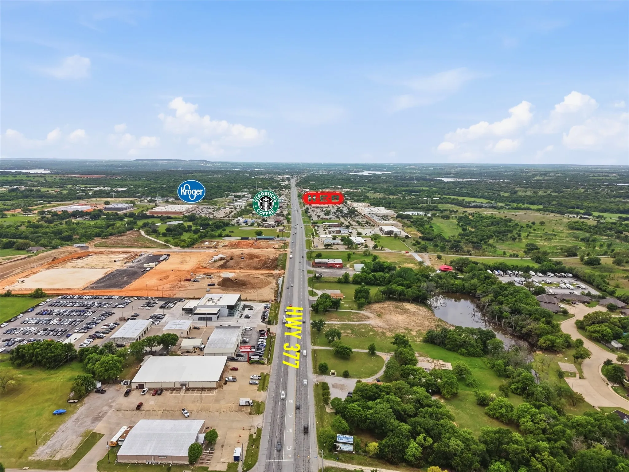 Aerial perspective showcasing commercial properties along a major highway, surrounded by green landscapes and bodies of water