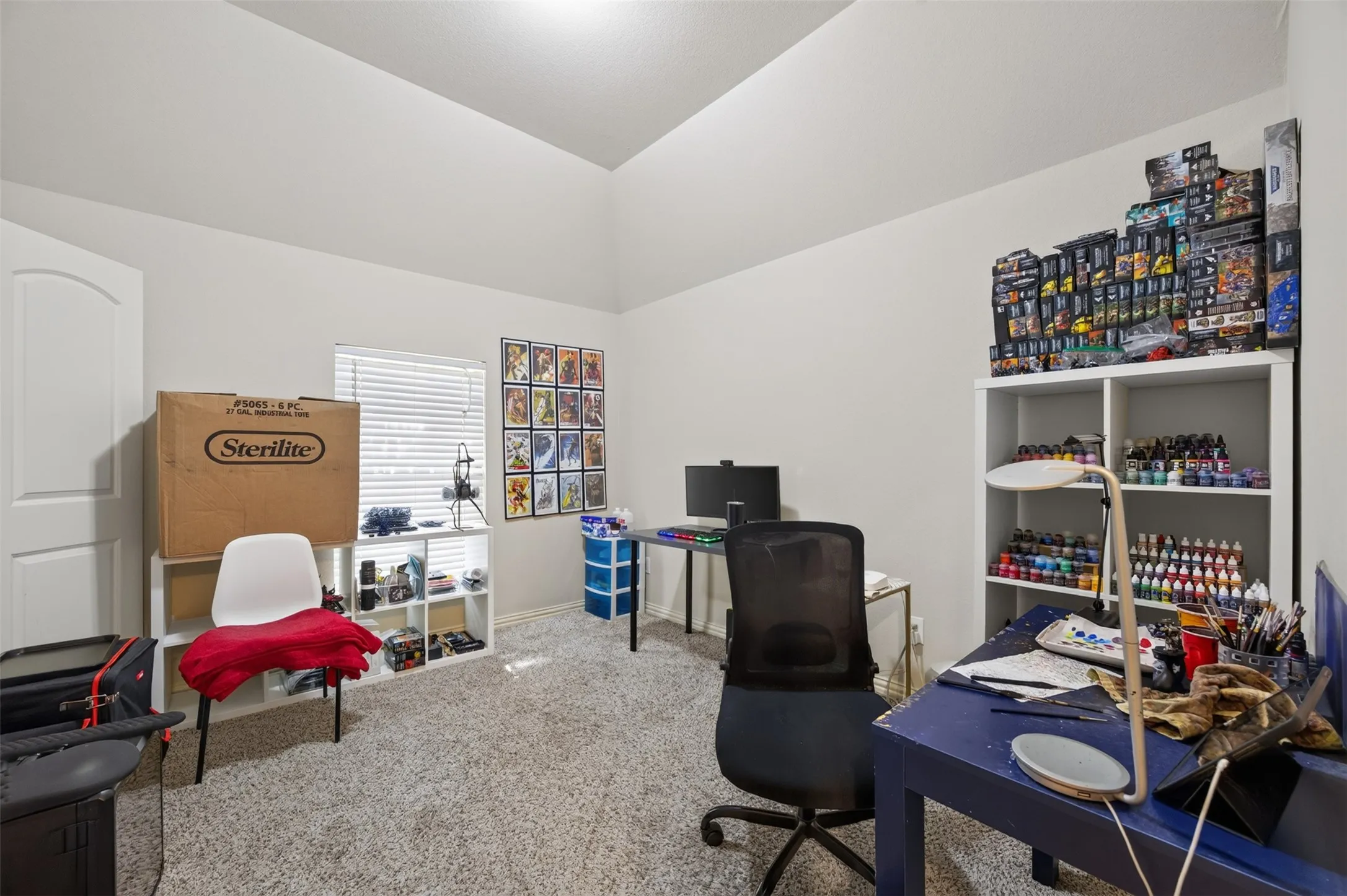 Vaulted ceiling with textured carpet flooring and a single window with blinds