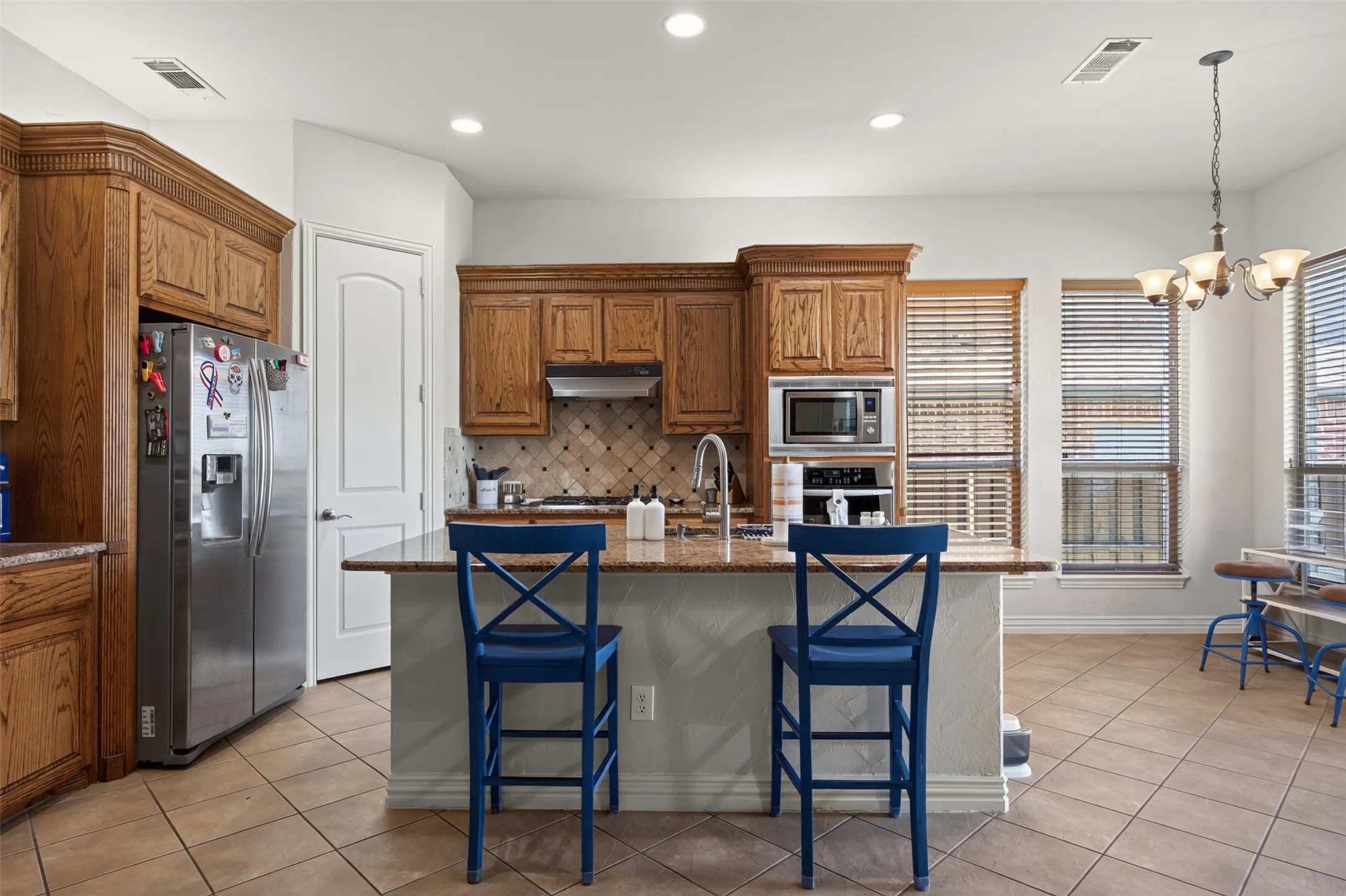 Kitchen featuring wood cabinetry, a built-in microwave, tile flooring, a center island with countertop seating, and multiple windows