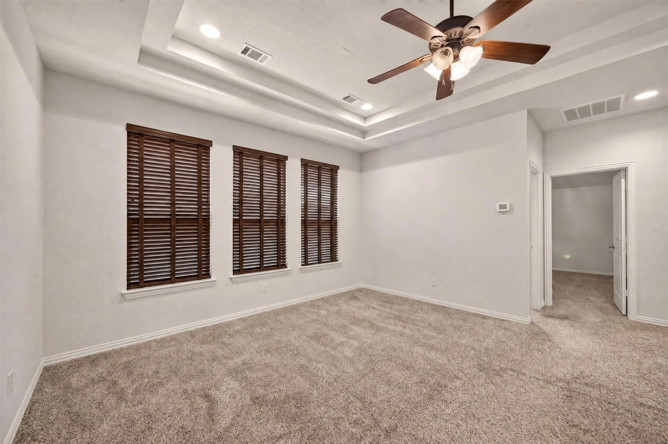 Tray ceiling with recessed lighting, ceiling fan with light fixture, three windows with wood blinds, and wall-to-wall carpeting