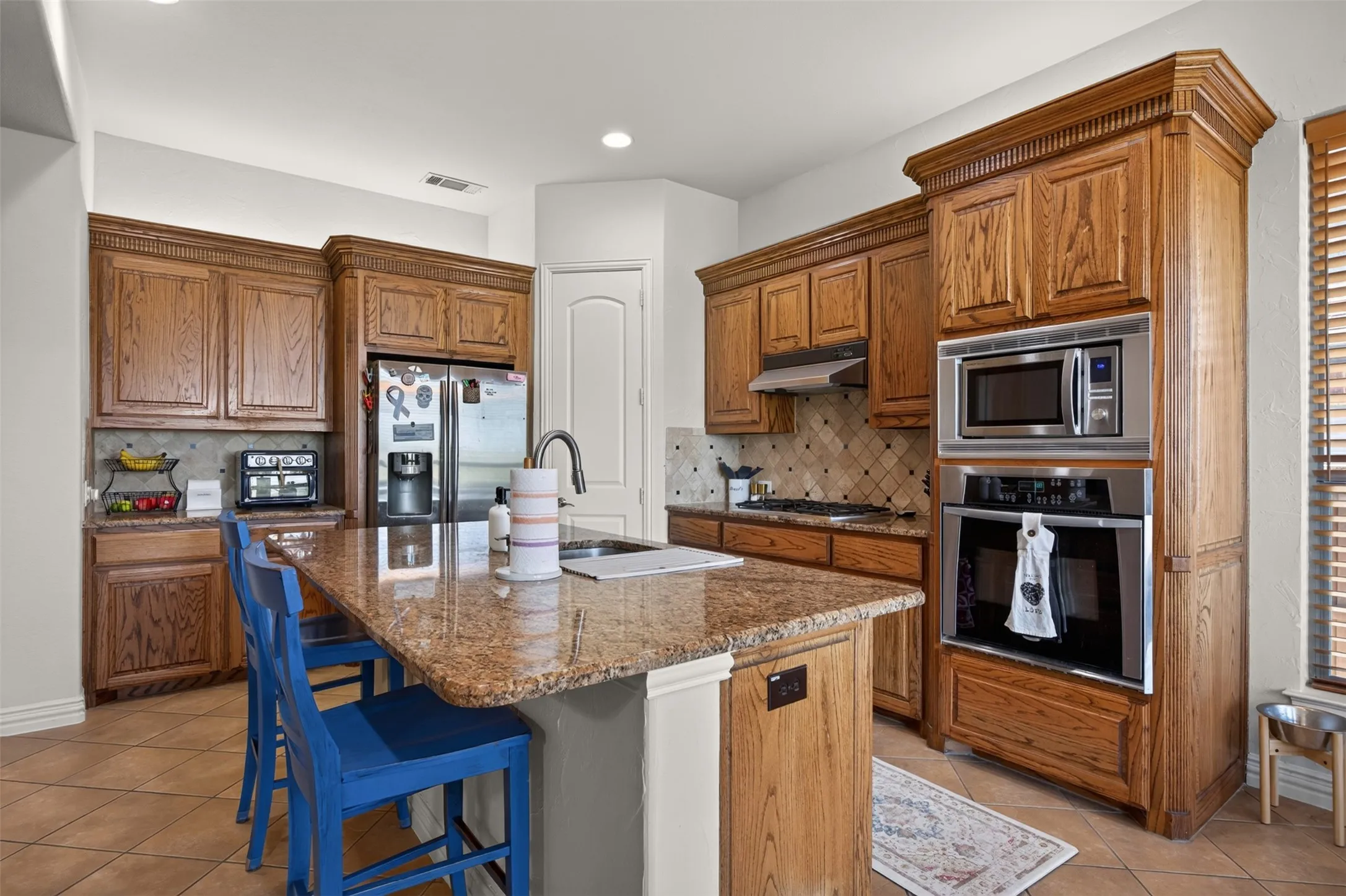 Kitchen featuring a center island with a granite countertop, built-in stainless steel appliances, wood cabinetry, and a tile backsplash