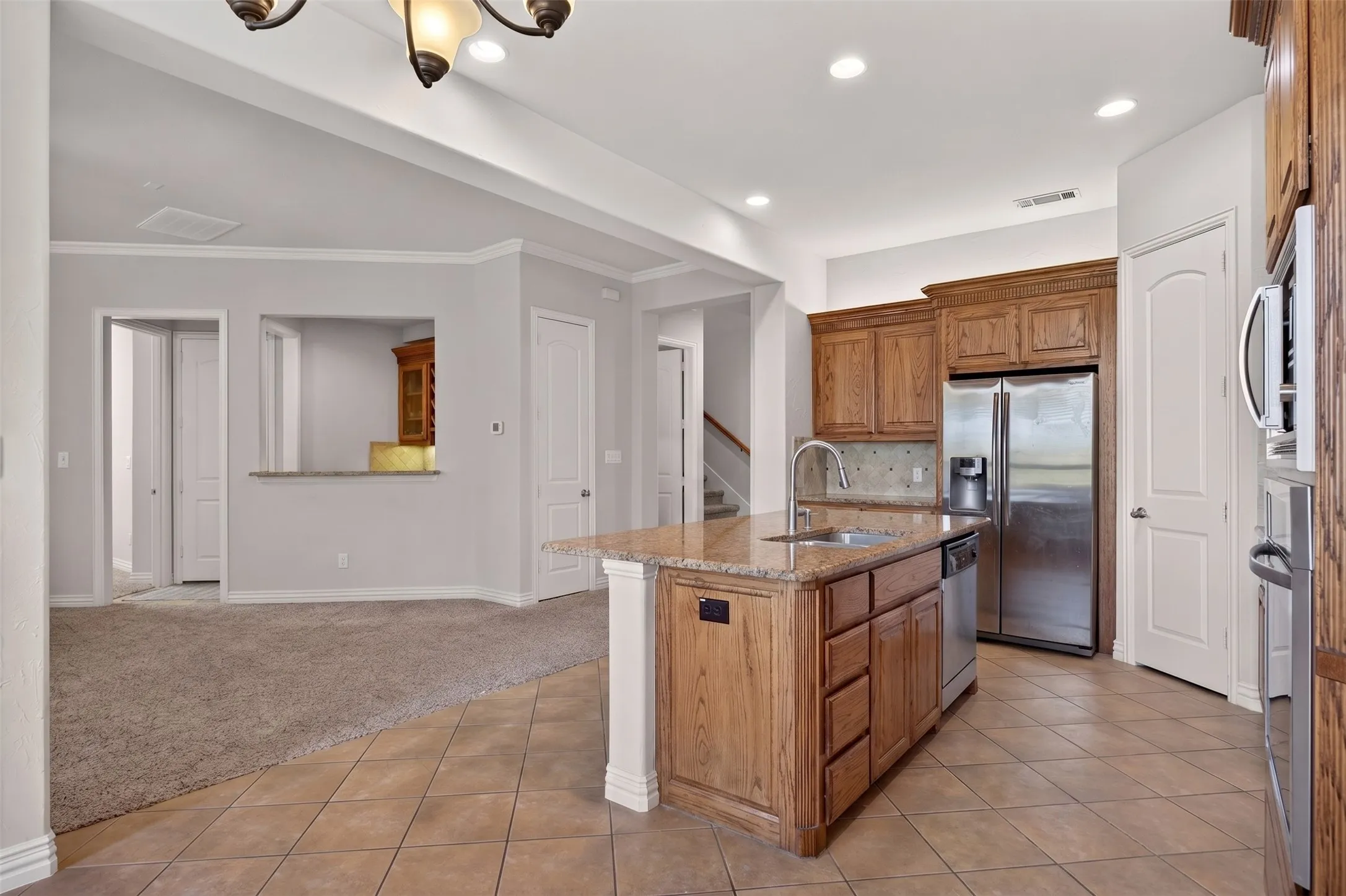 Kitchen featuring a center island with sink, granite countertops, wood cabinetry, stainless steel appliances, and tiled flooring