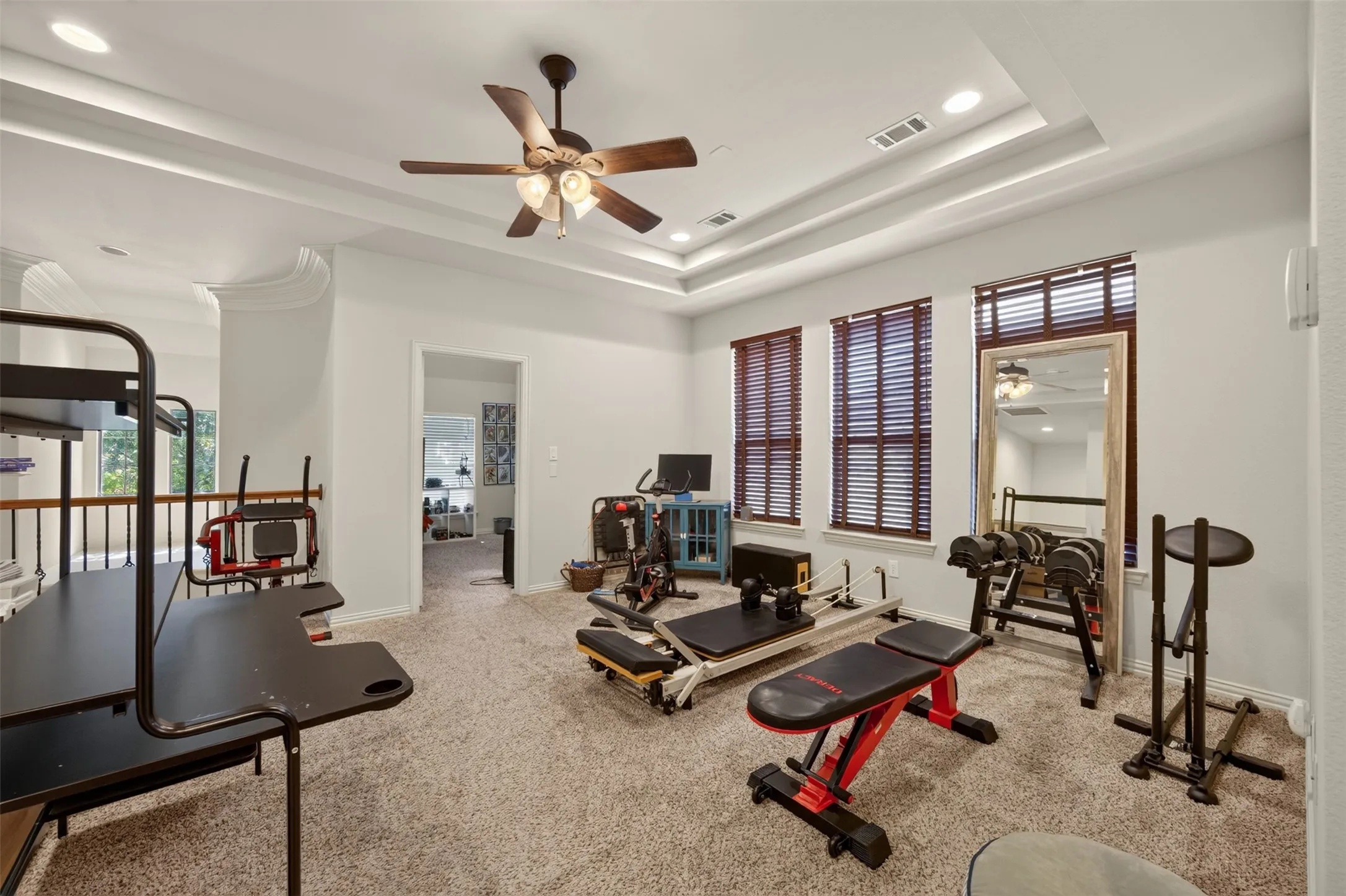 Tray ceiling with recessed lighting, brown ceiling fan, three windows with wood blinds, and wall-to-wall carpeting
