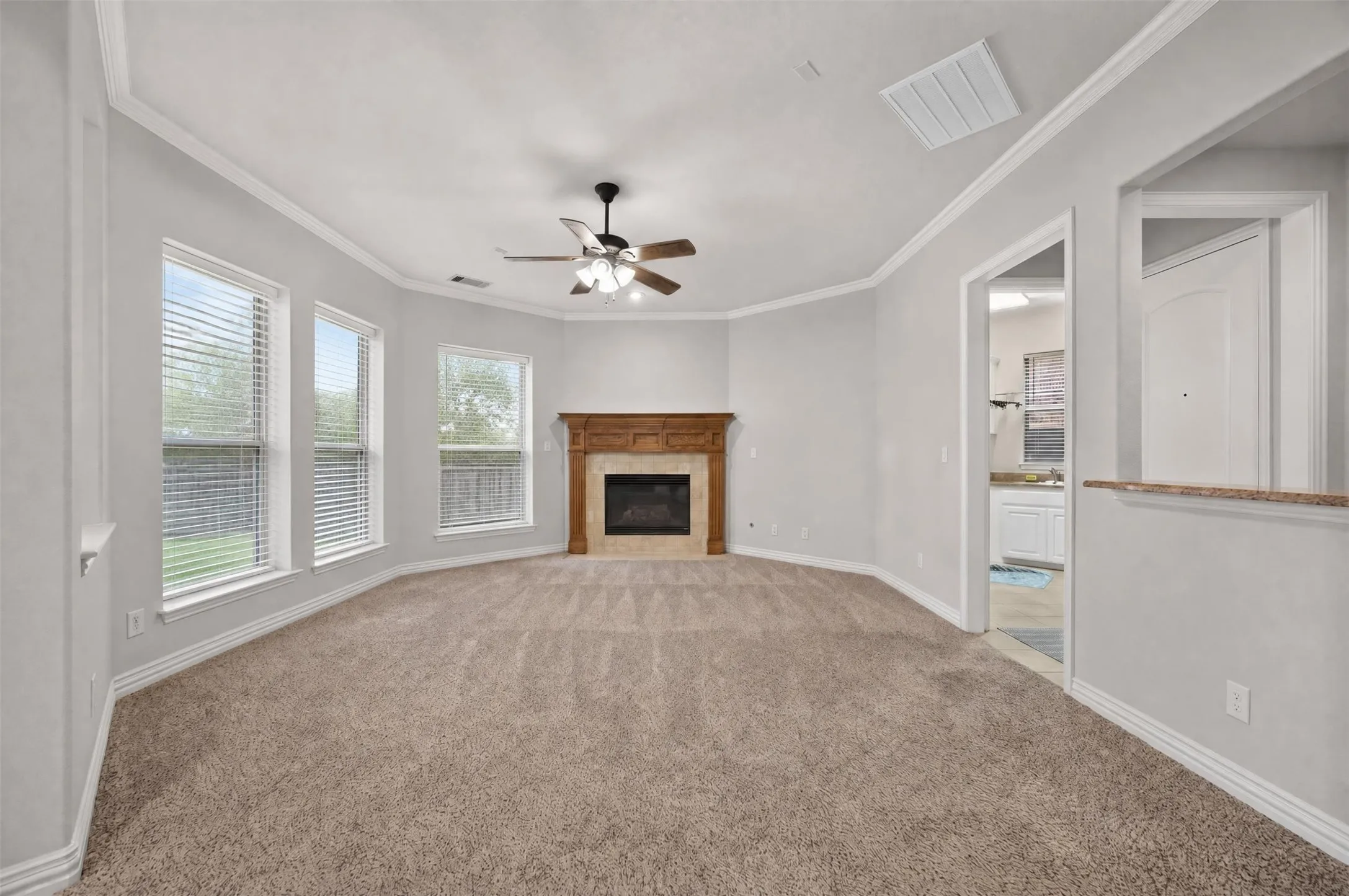 Neutral tone wall color, ceiling fan with light fixture, decorative wood fireplace surround, recessed fireplace insert, and multiple windows