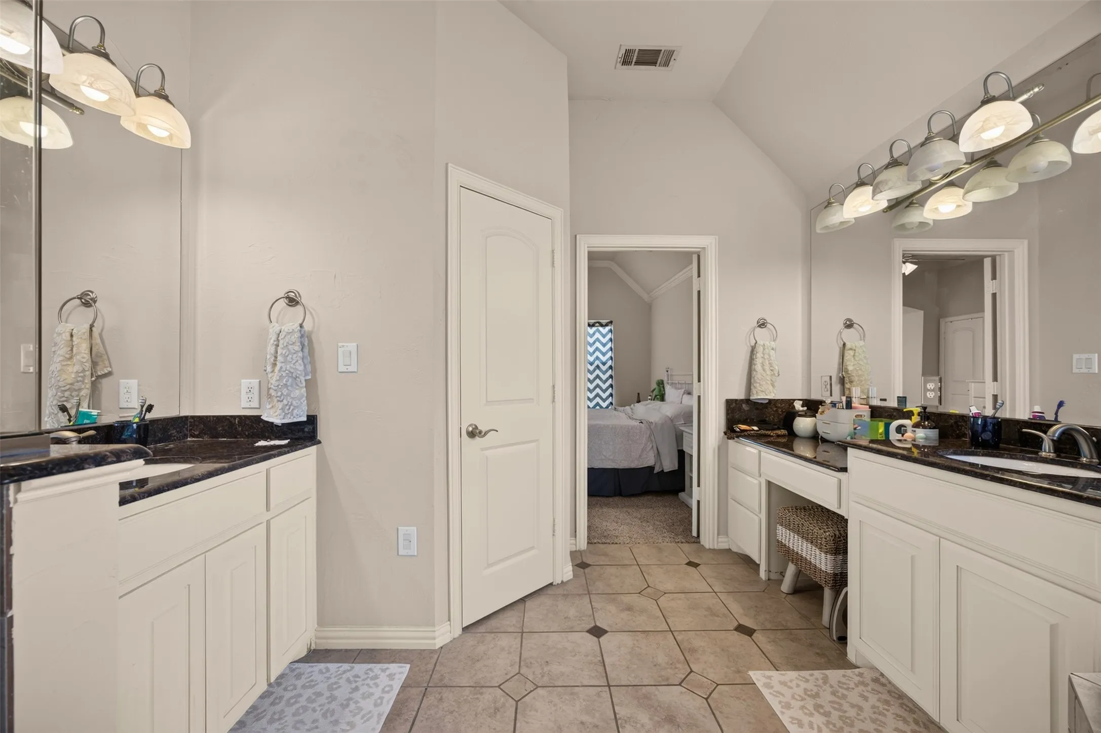 Dual vanity with white cabinetry and dark countertops, tile flooring, and vaulted ceiling
