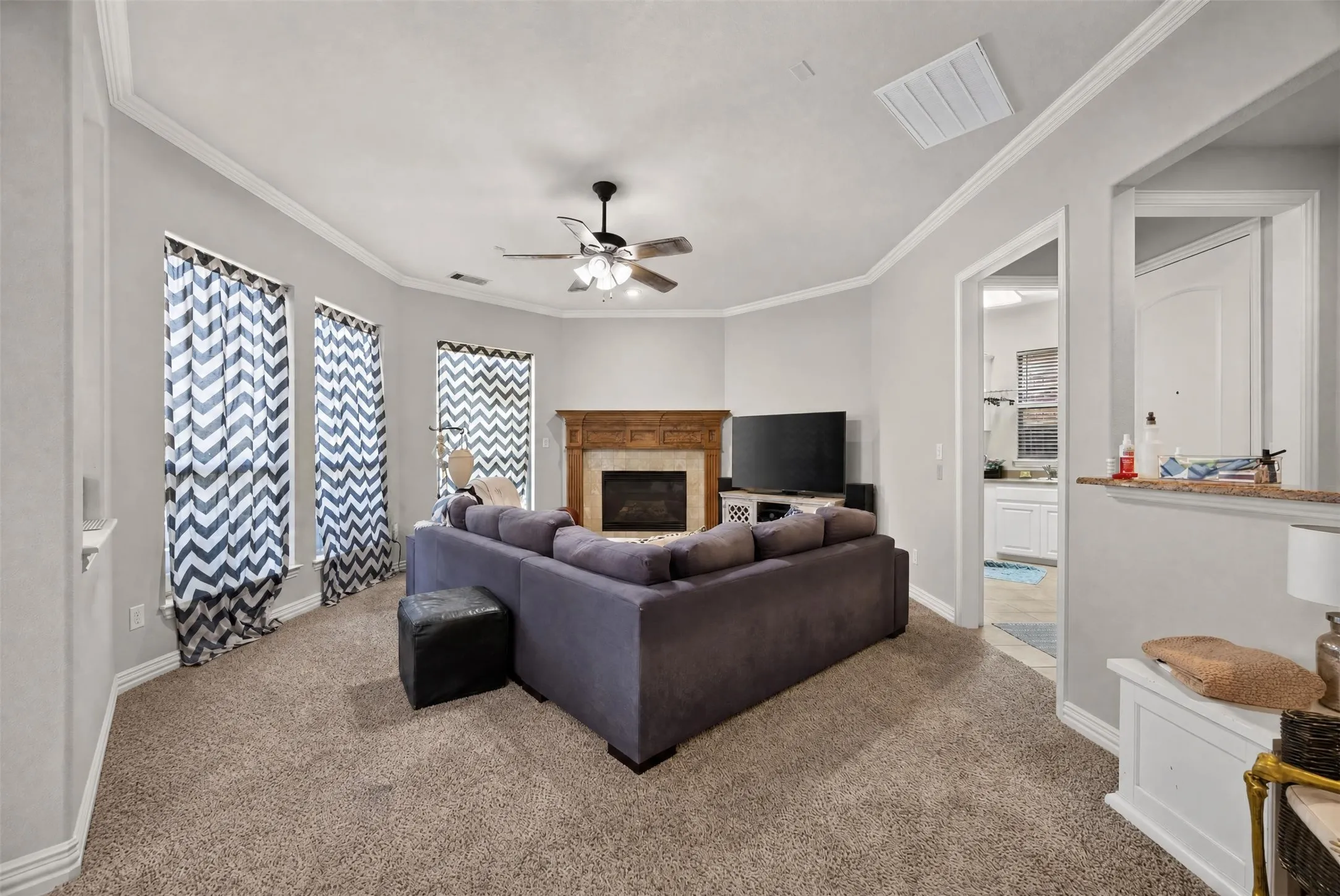 Carpeted living area featuring crown molding, a ceiling fan, and a fireplace with a wood-finish mantel