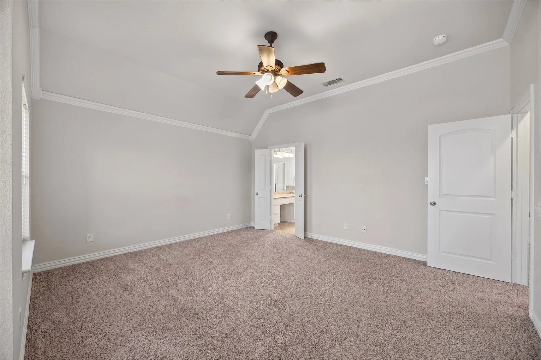 Vaulted ceiling with crown molding, ceiling fan, and plush carpeting