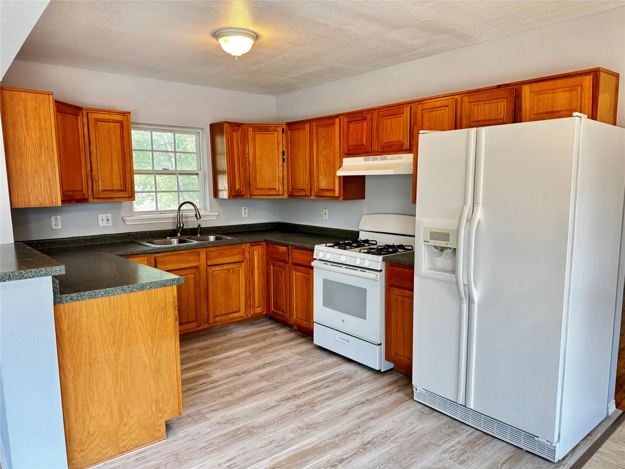 Kitchen featuring wood-finish cabinetry, dark countertops, a double basin sink with a high-arc faucet, and wood-finish flooring