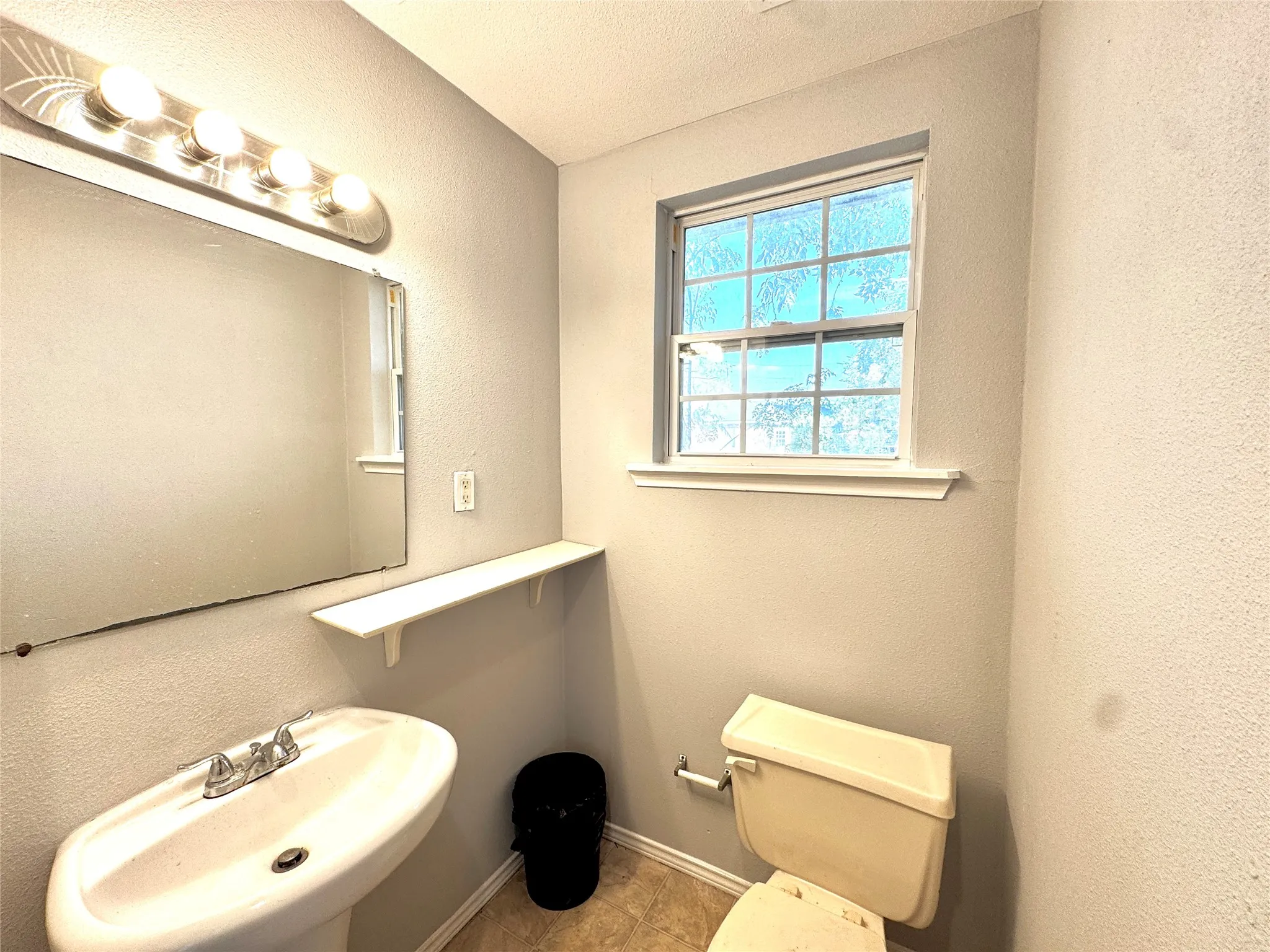 Pedestal sink with chrome-finish faucet, wall-mounted mirror, and vanity light fixture