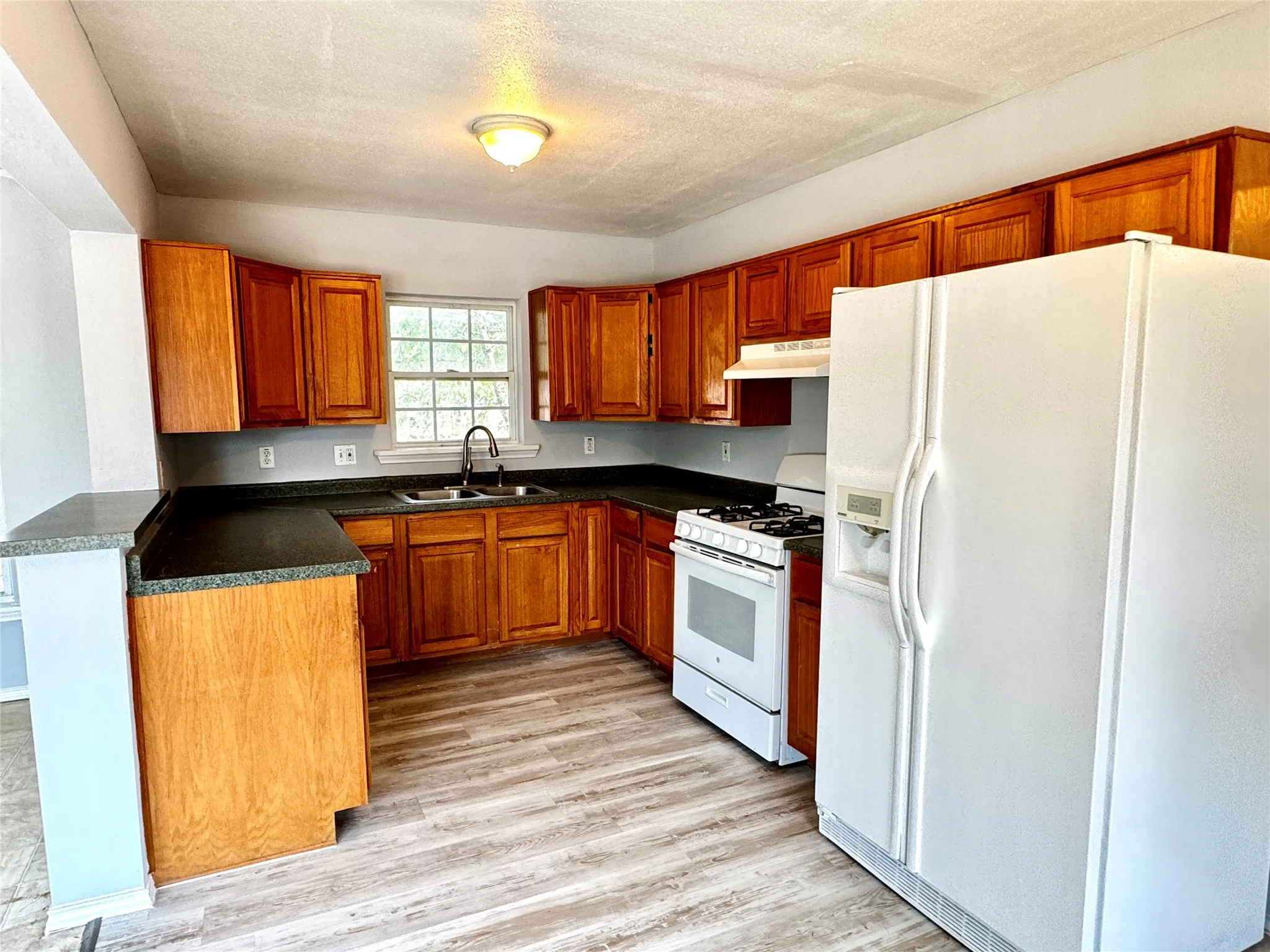 Kitchen featuring wood-finish cabinetry, dark countertops, a double basin sink with a gooseneck faucet, a white range with an oven, and wood-finish flooring