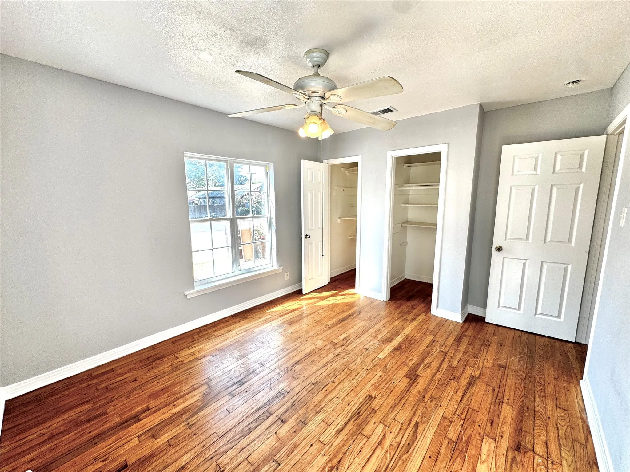 Wood-finish flooring, ceiling fan with integrated lighting, window with white trim, and two built-in closets with shelving