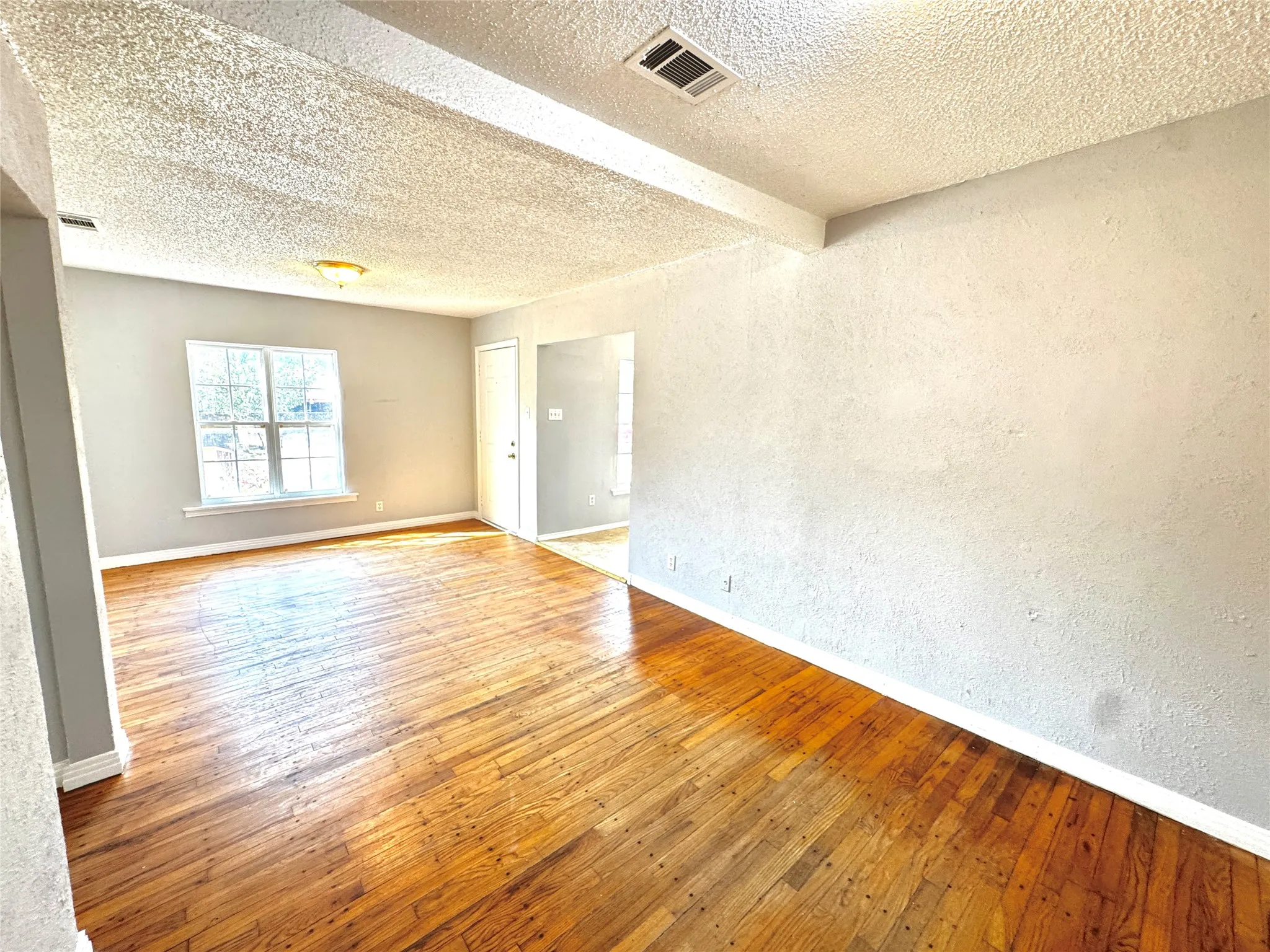 Hardwood flooring, painted walls, white trim, window with multiple panes, and ceiling-mounted light fixture
