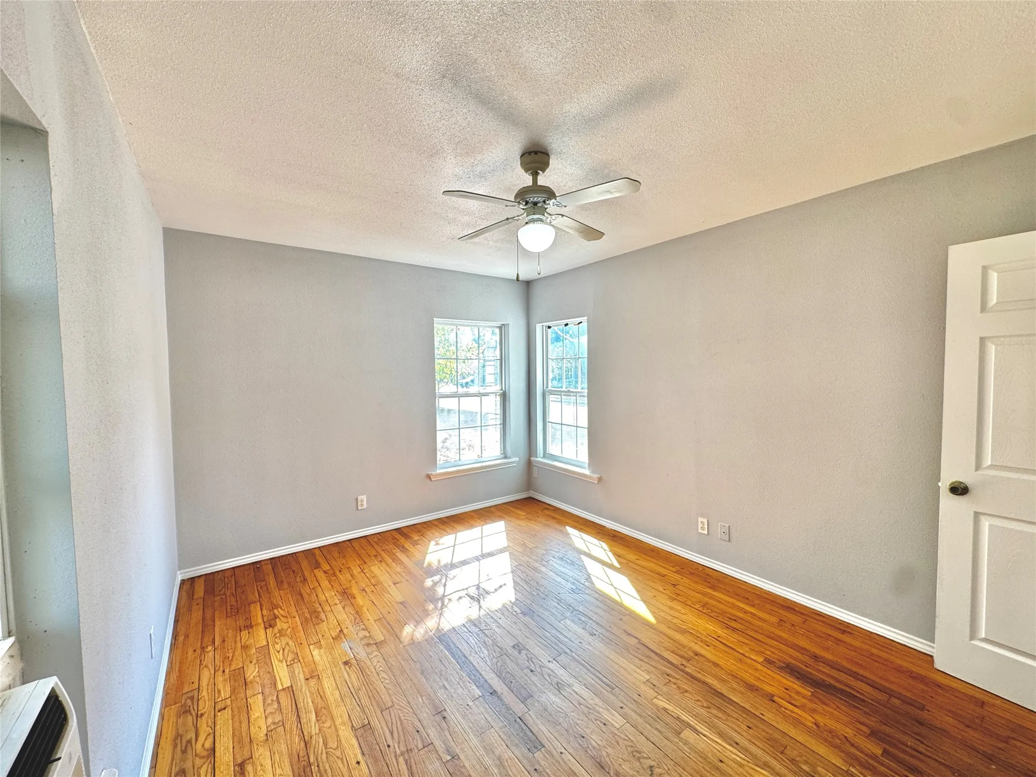 Hardwood flooring, painted walls, ceiling fan with integrated lighting, multiple windows, and a panel door