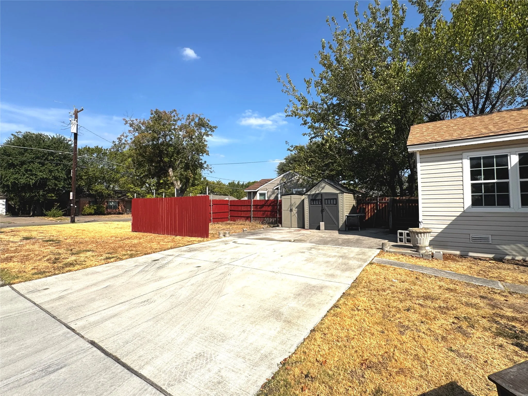 Expansive concrete driveway, detached storage shed, wood fence, light-colored siding, and multi-pane window