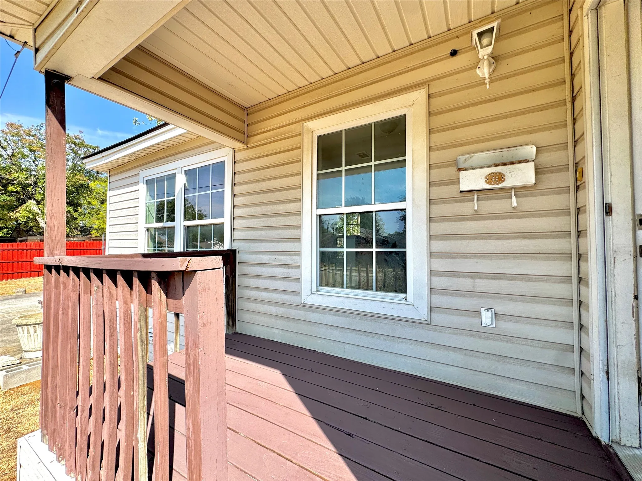 Covered porch with wood-finish decking, vertical wood railings, and two windows featuring grid panes