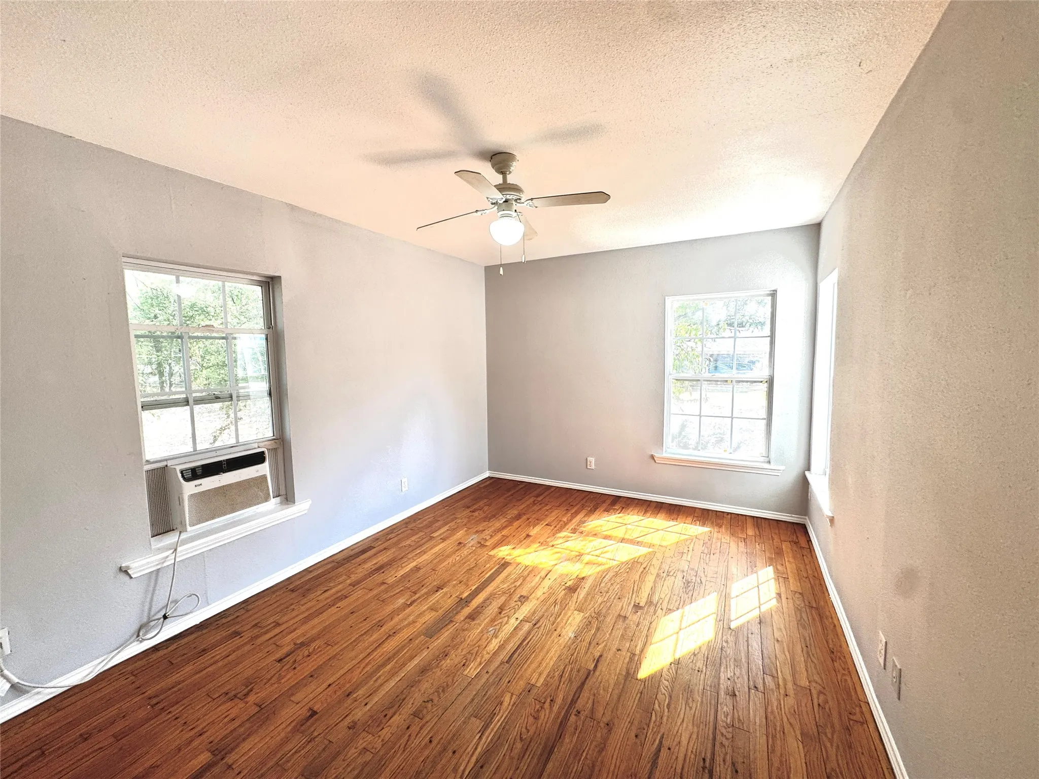 Refinished wood flooring, ceiling fan with integrated lighting, multiple windows, and light gray wall finishes