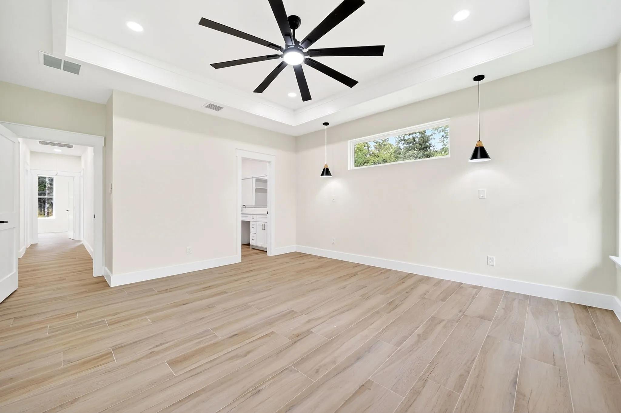 Spacious room featuring wood-finish flooring, a tray ceiling with a ceiling fan, recessed lighting, and two pendant lights