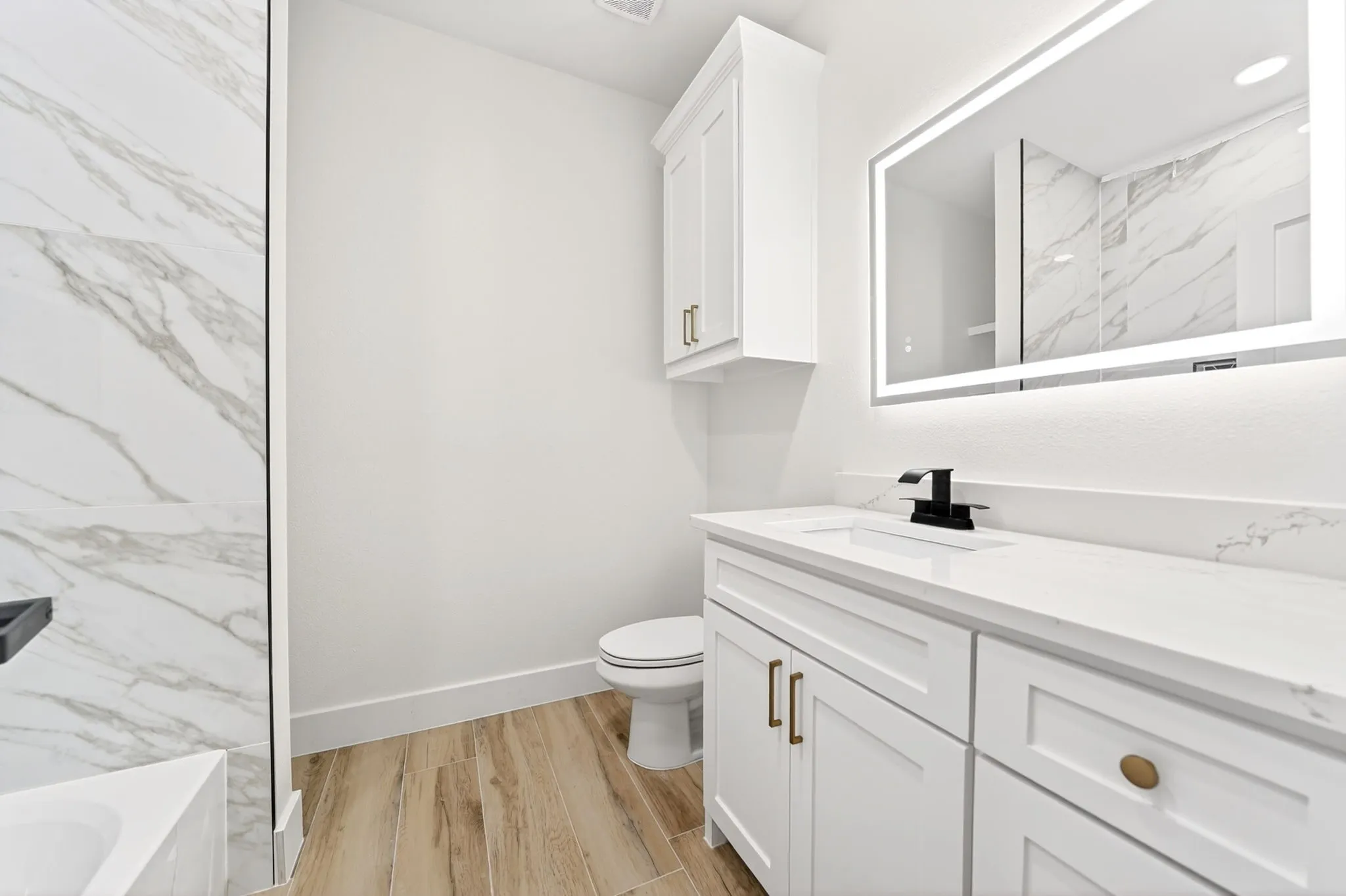White vanity with a solid surface countertop, matte black faucet, and an illuminated mirror