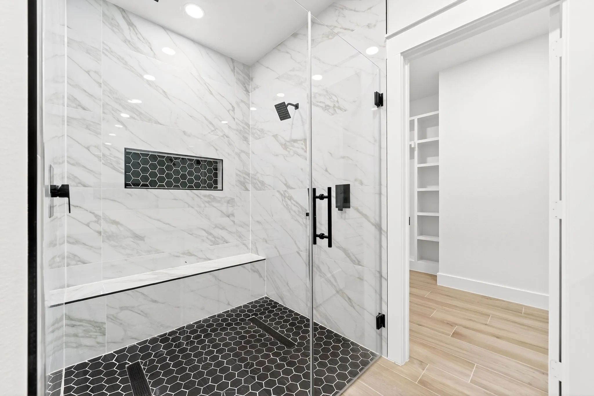 Glass-enclosed shower featuring white marble-finish tiling, matte black fixtures, a built-in bench, and a hexagonal tiled floor