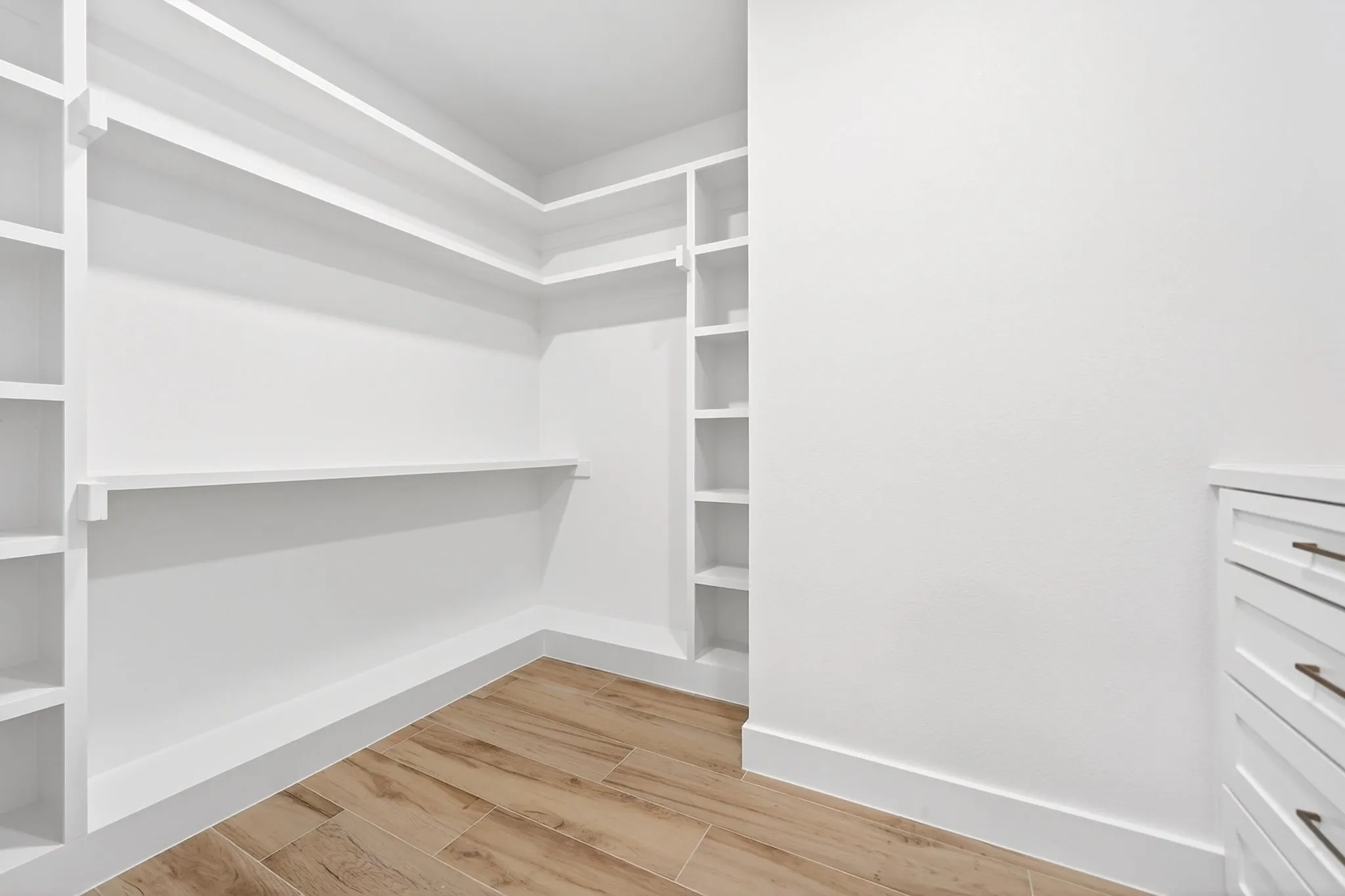 Built-in closet shelving and storage, wood-finish flooring, and white cabinetry with drawer pulls