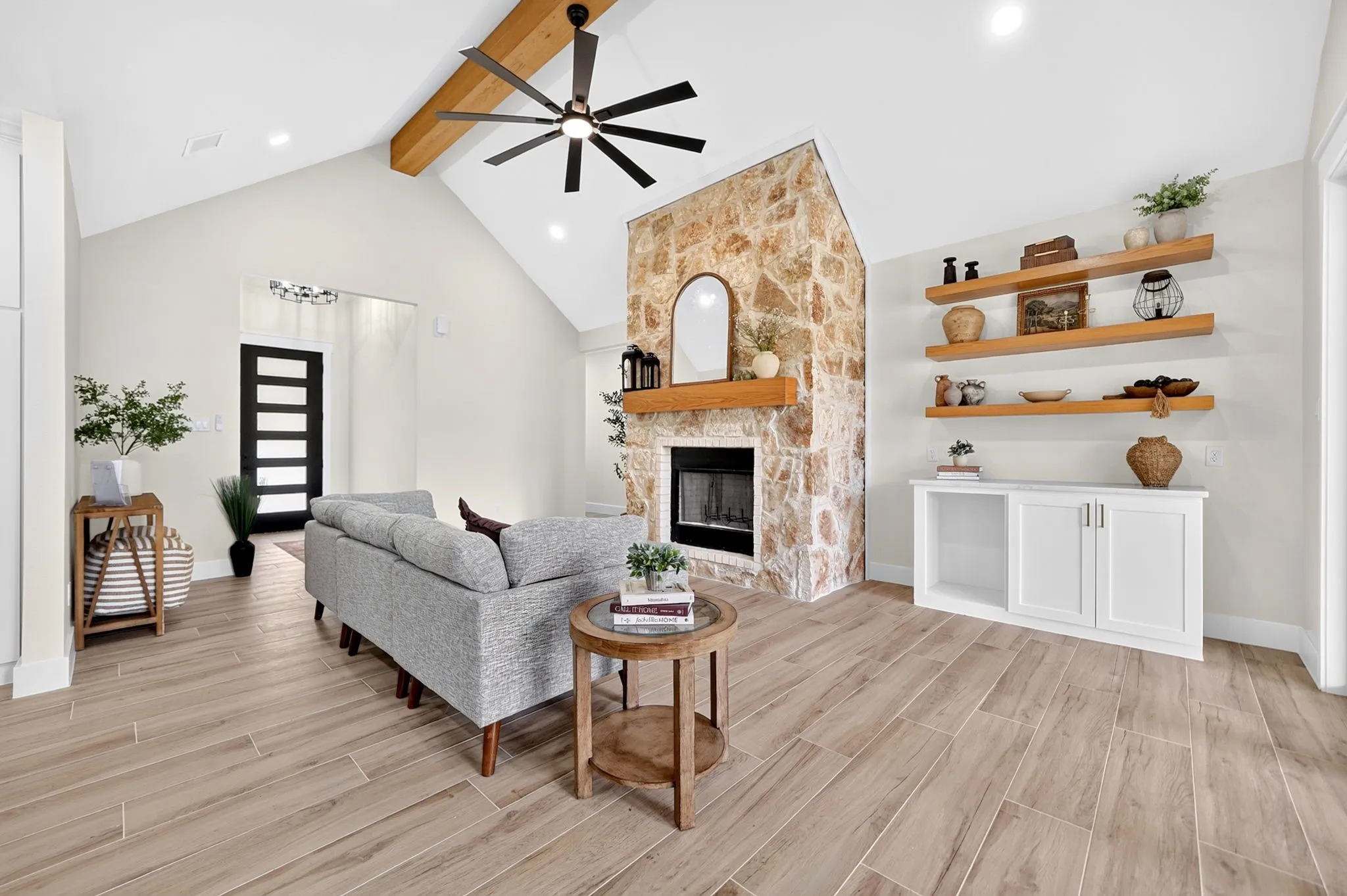 Vaulted ceiling with exposed wood beam, stone-surround fireplace with wood mantel, wood-finish flooring, built-in shelving, and recessed lighting