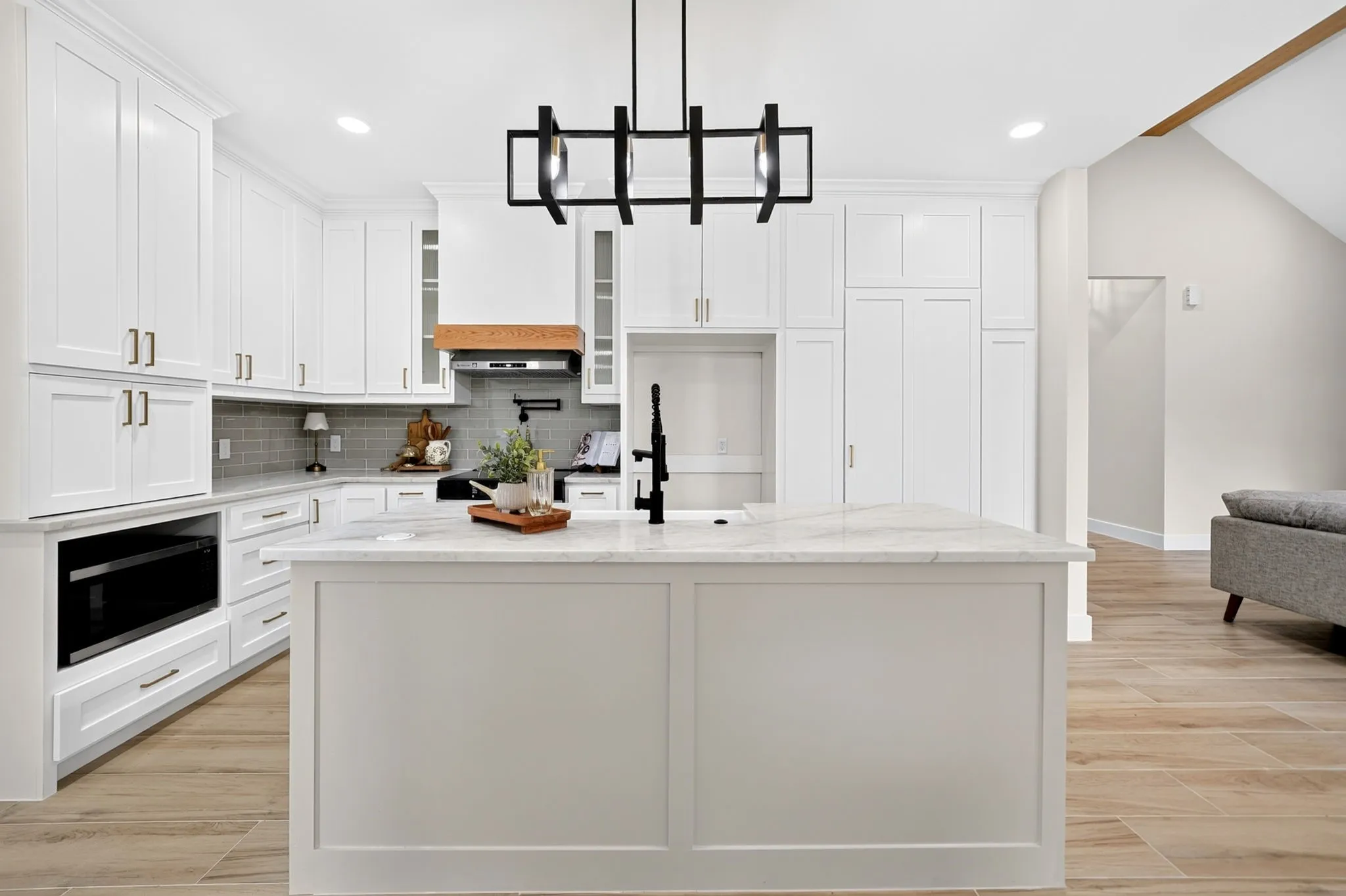 White shaker cabinetry with gold-toned hardware, center island featuring a white stone countertop, wood-finish flooring, and a contemporary black chandelier