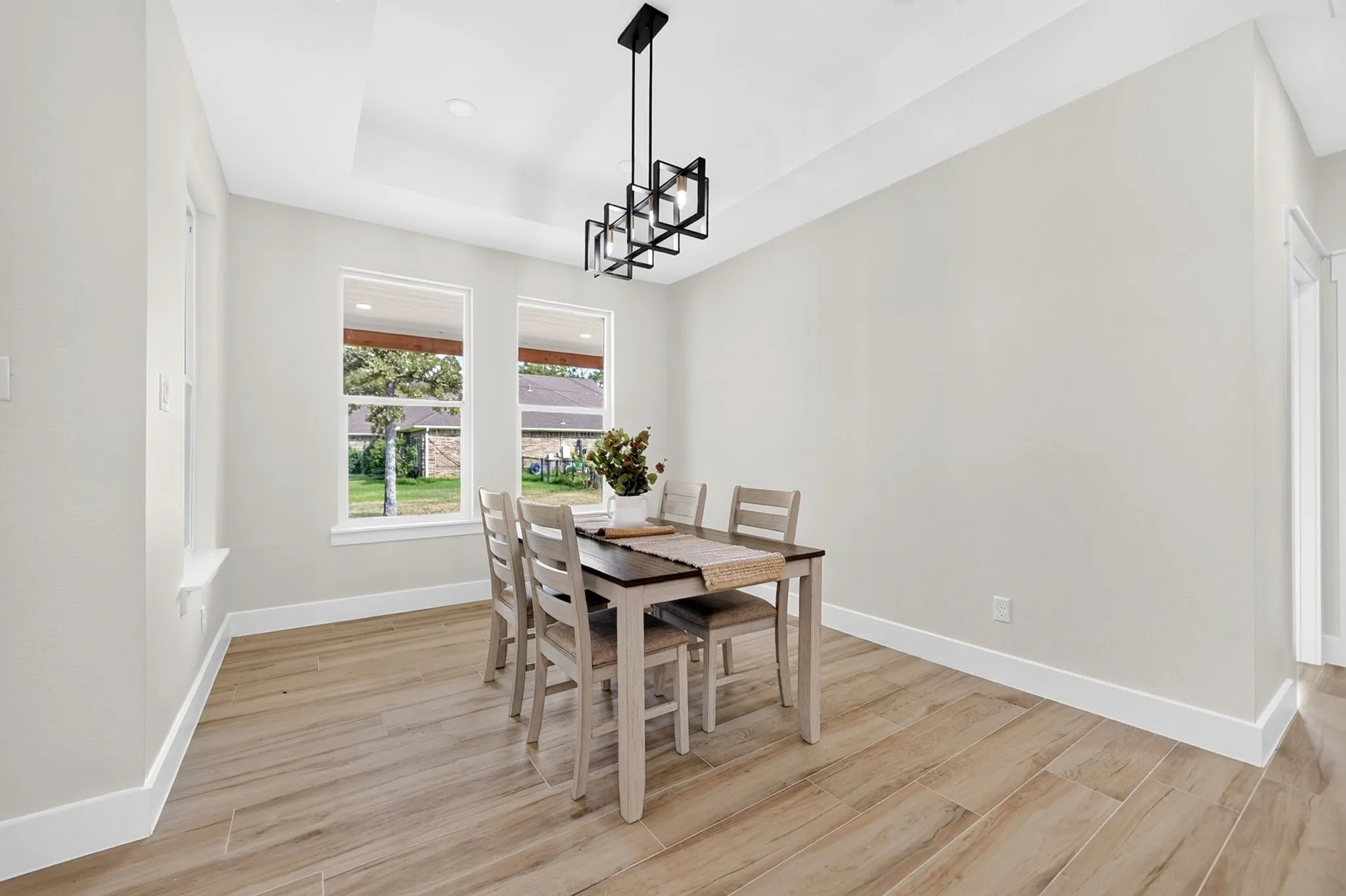 Tray ceiling with a contemporary black linear chandelier, wood-finish flooring, and multiple windows